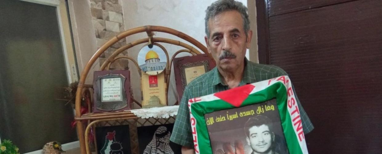 حسن دولة يحمل صورة شقيقه الأسير الشهيد أنيس المحتجز جثمانه منذ استشهاده في السجن الإسرائيلي عام 1980. (الجزيرة)